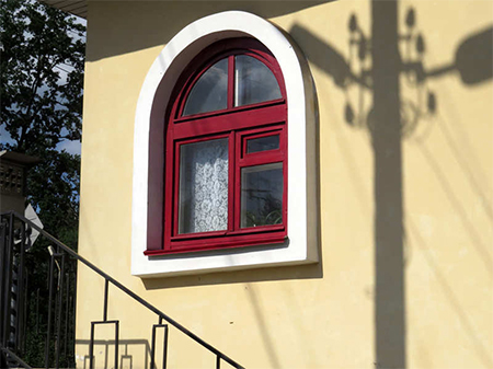 rotes Segmentfogenfenster in einer gelben Fassade verbaut